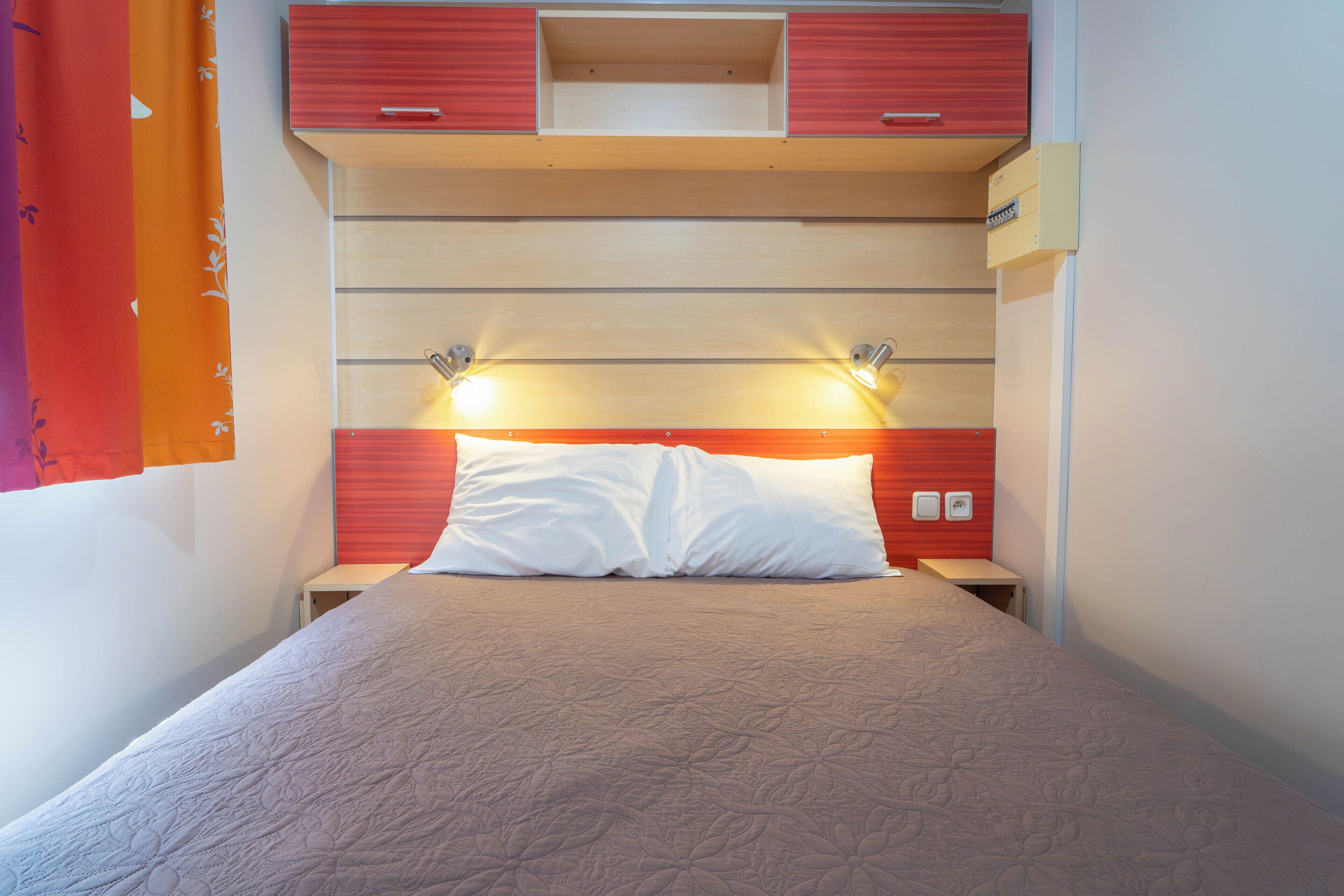 Un dormitorio con una cama, dos lámparas de noche, una mesita de noche y un cabecero rojo y beige.