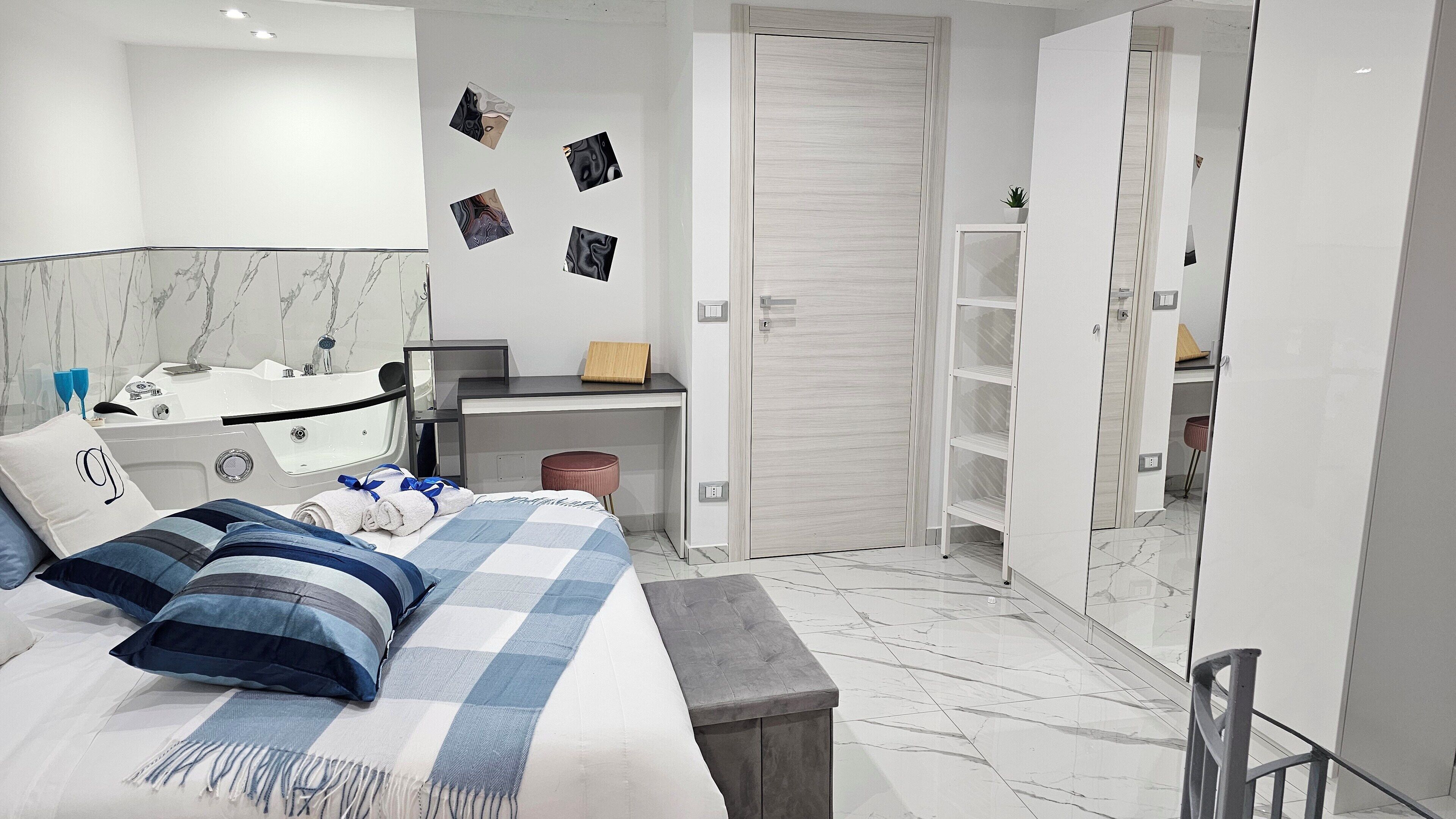 A modern bedroom with a bed, a desk, a vanity, a wardrobe, and a bathroom.