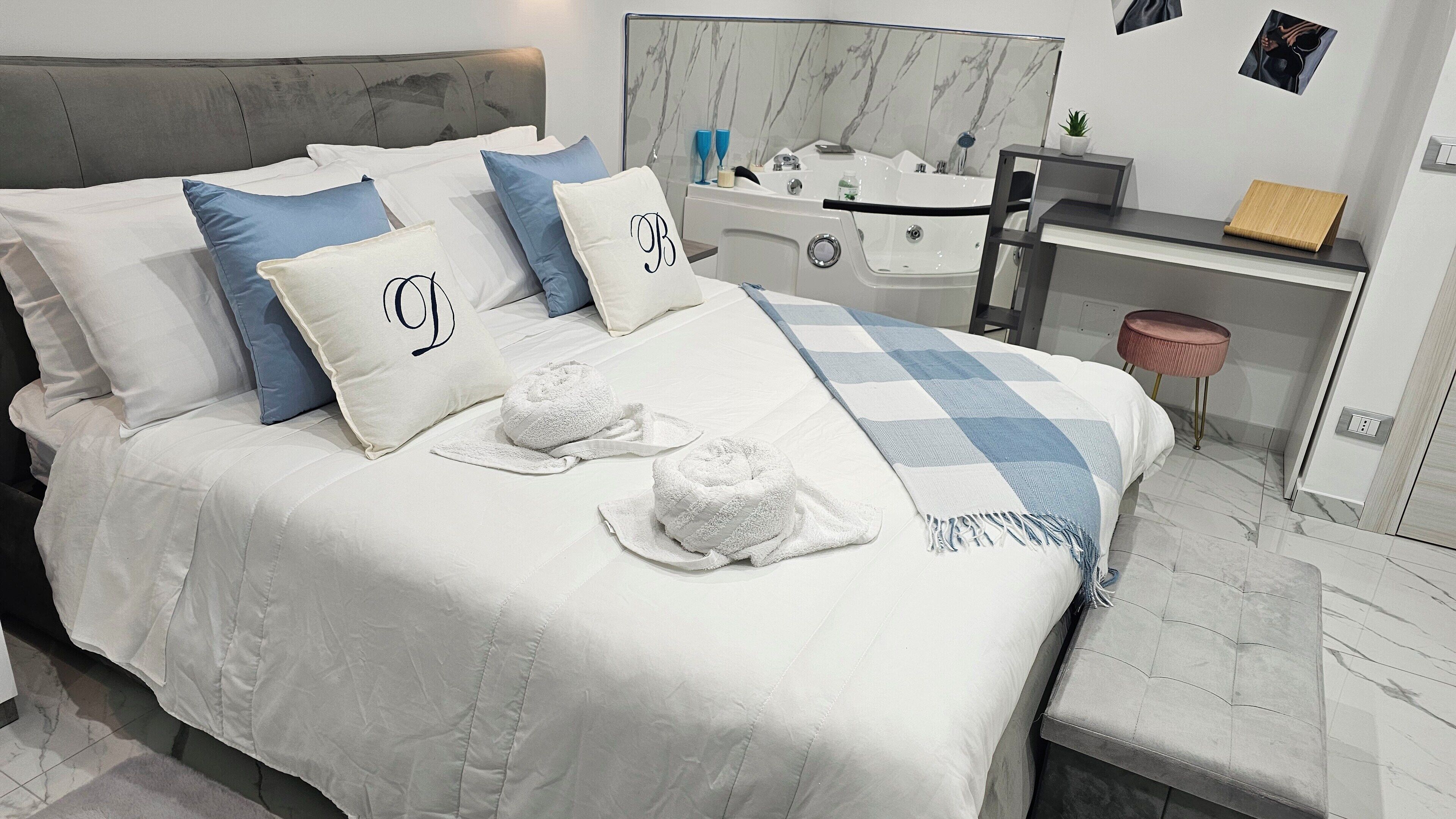 Una cama bien hecha con ropa blanca, dos toallas y almohadas con iniciales.