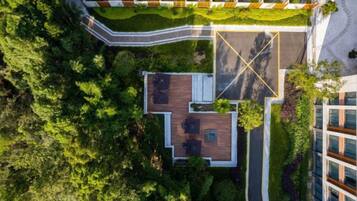 An aerial view of a building with a rooftop terrace, surrounded by greenery and adjacent to a road.