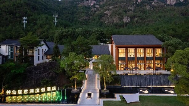 Un hotel moderno con una amplia fachada de vidrio, rodeado por un jardín ajardinado y una cascada.