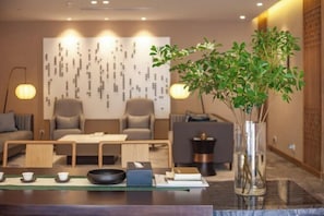 A modern hotel room with a minimalist decor, featuring a sofa, a coffee table, and a decorative plant in a vase.