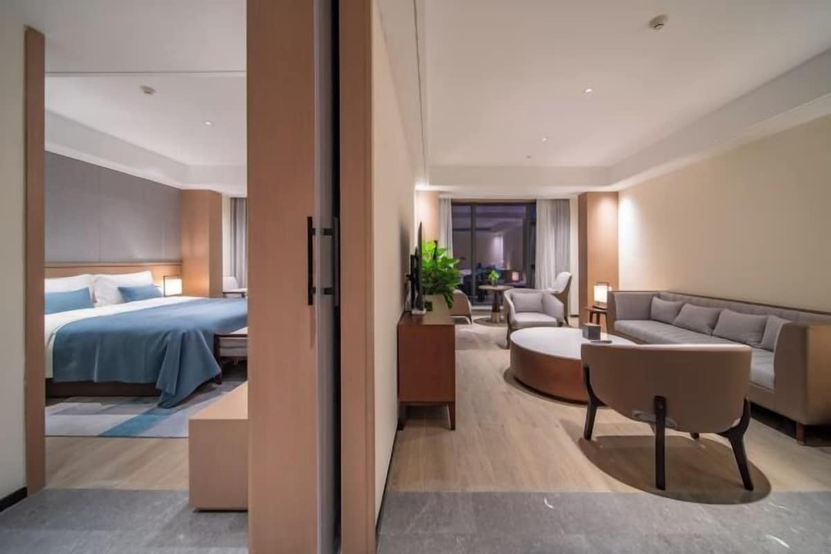 A modern hotel room with a bed, a sofa, a coffee table, and a desk.