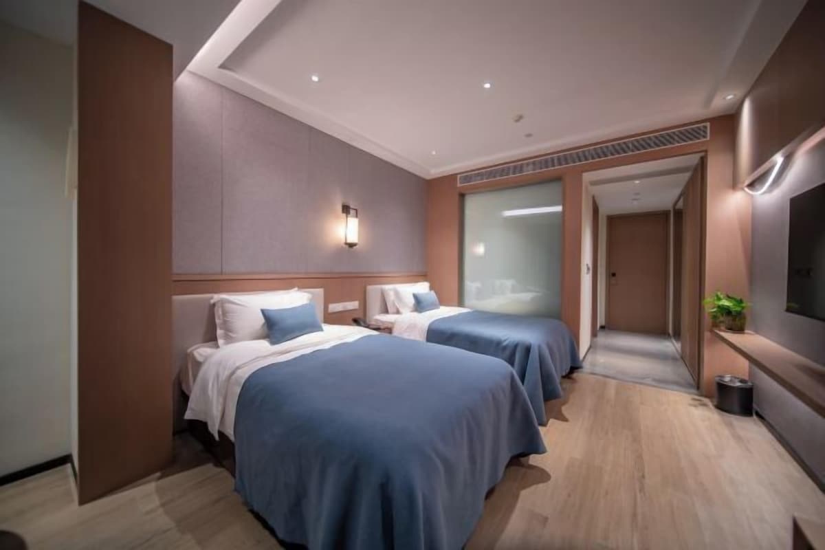A hotel room with two beds, a large mirror, a TV, and a plant.