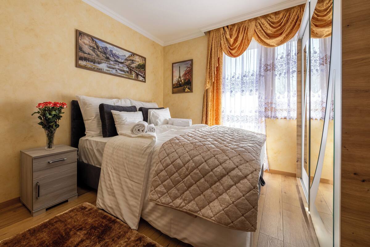 A neatly arranged bedroom with a bed, a nightstand, a vase of flowers, and two paintings on the wall.