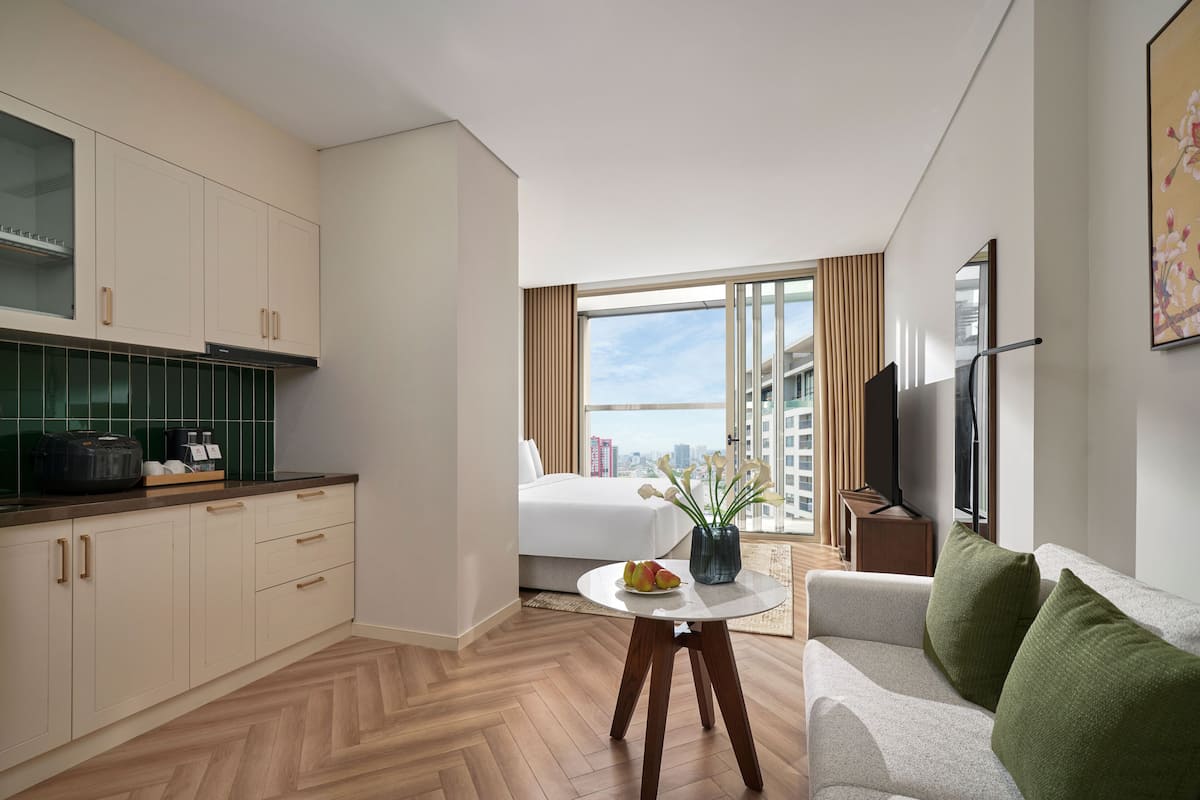 Habitación de hotel moderna con kitchenette, una mesa de comedor, un sofá y un ventanal con vista a la ciudad.