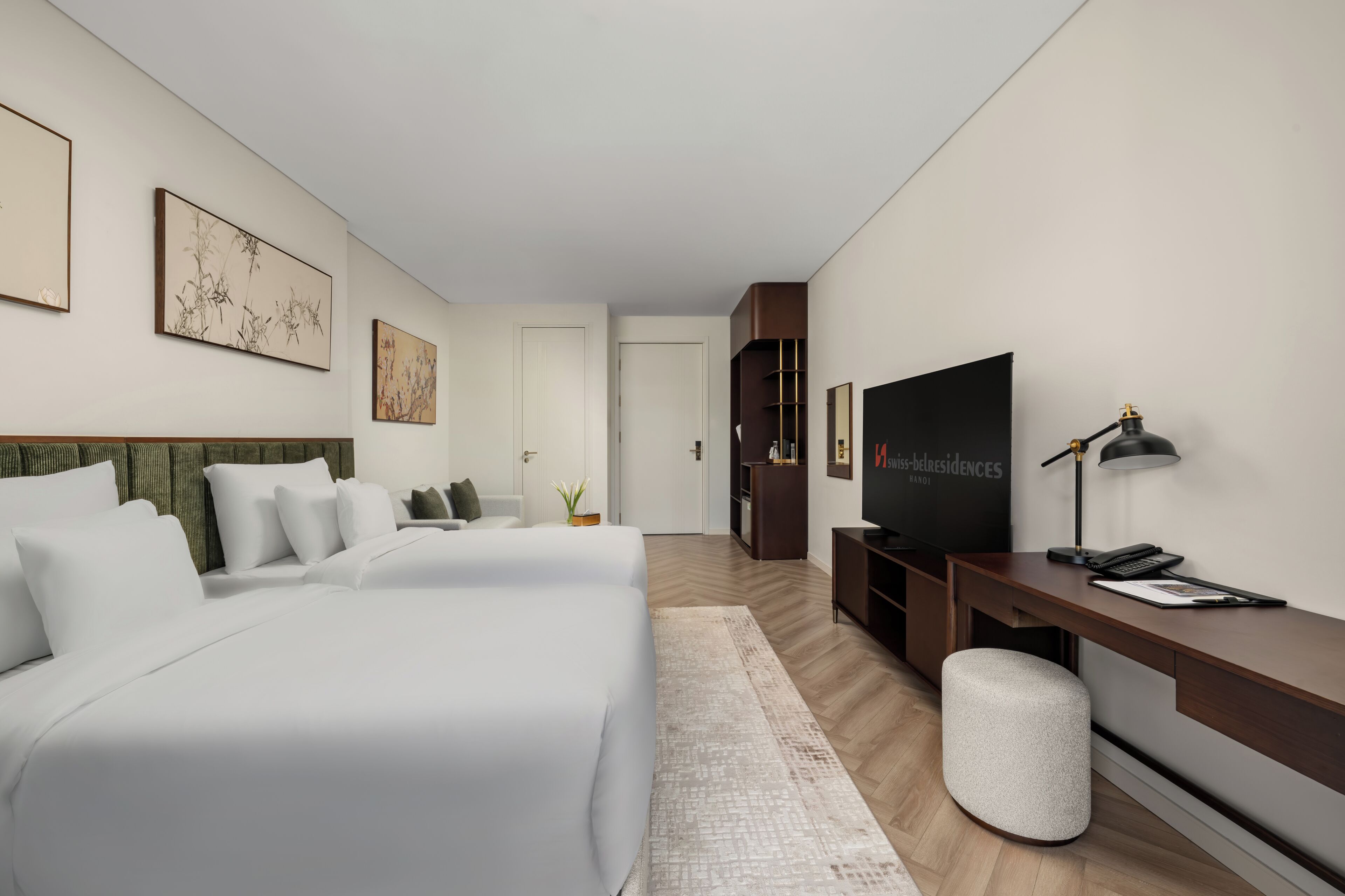 A modern hotel room with a large bed, a desk with a computer, a TV, and artwork on the walls.