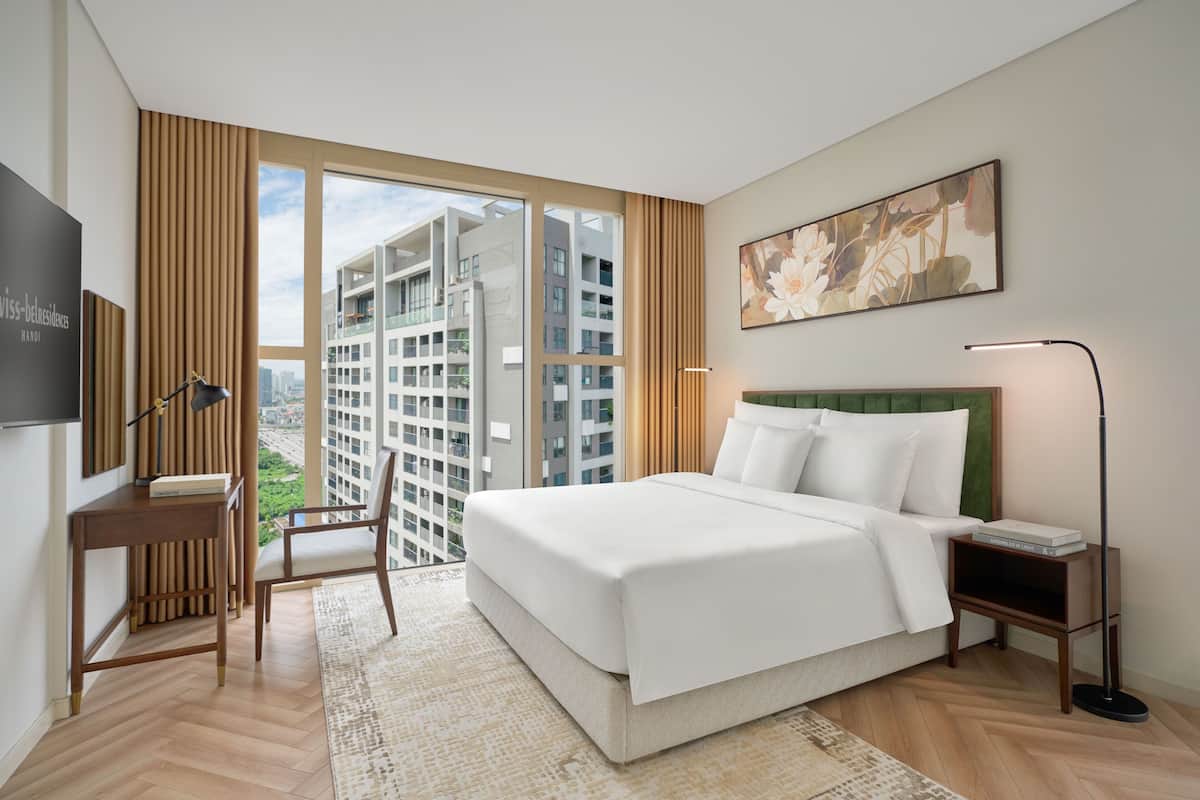 Habitación de hotel con una cama grande, un escritorio, una silla, un televisor y una ventana con vistas a la ciudad.