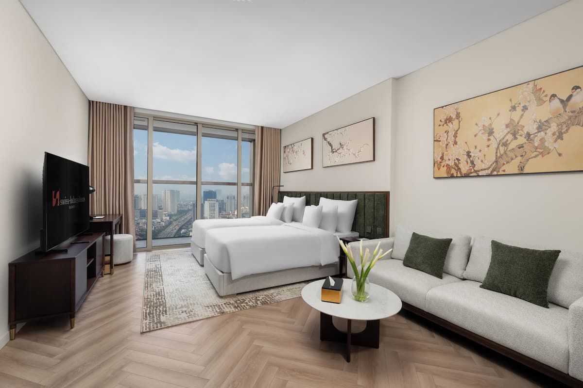 Una habitación de hotel moderna con una cama grande, un sofá, un televisor y vistas a la ciudad.