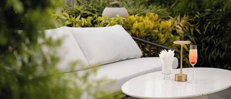 A white outdoor seating area with a round table, two glasses of drink, and a white napkin holder.