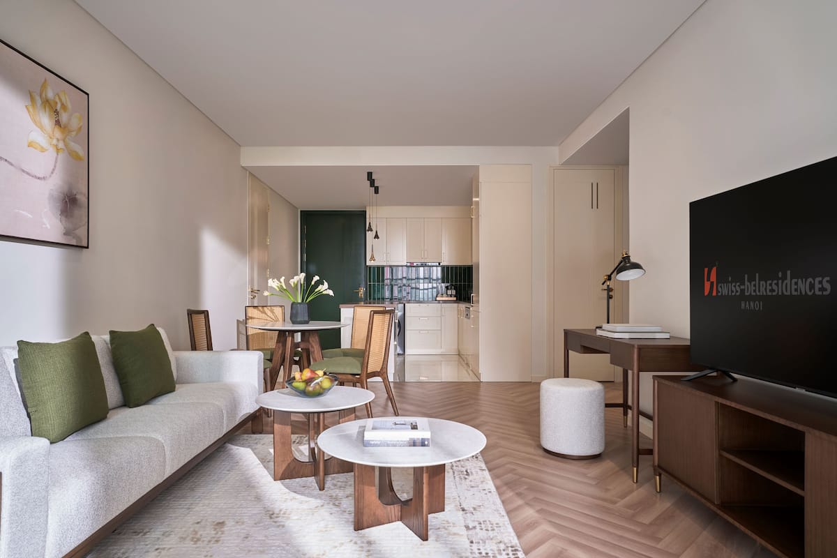 Una sala moderna con sofá, mesa de centro y mueble para la televisión. Hay una zona de comedor con una mesa y sillas, y una cocina al fondo.