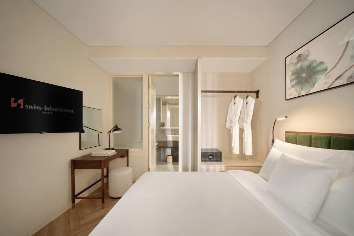 A hotel room with a bed, a desk, a chair, a wardrobe, and a shower area.