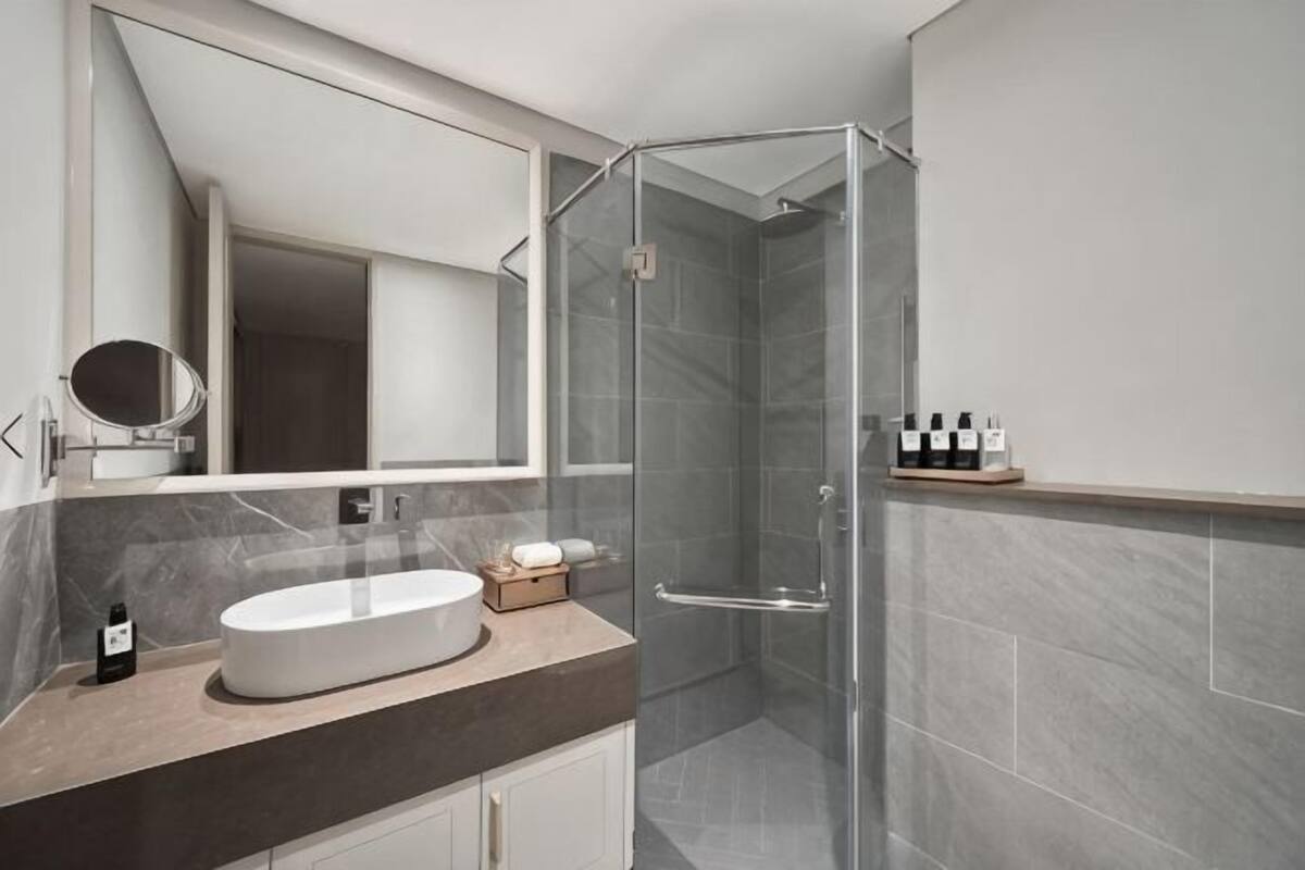 Un baño moderno con cabina de ducha de vidrio, un espejo redondo y encimera de mármol.