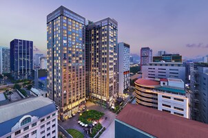 Un moderno edificio de gran altura con fachada de vidrio, rodeado de otros edificios altos en un entorno urbano.