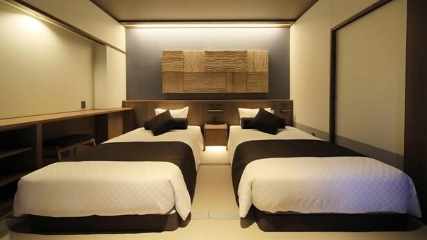 Een hotelkamer met twee bedden, een bureau en een wandpaneel.