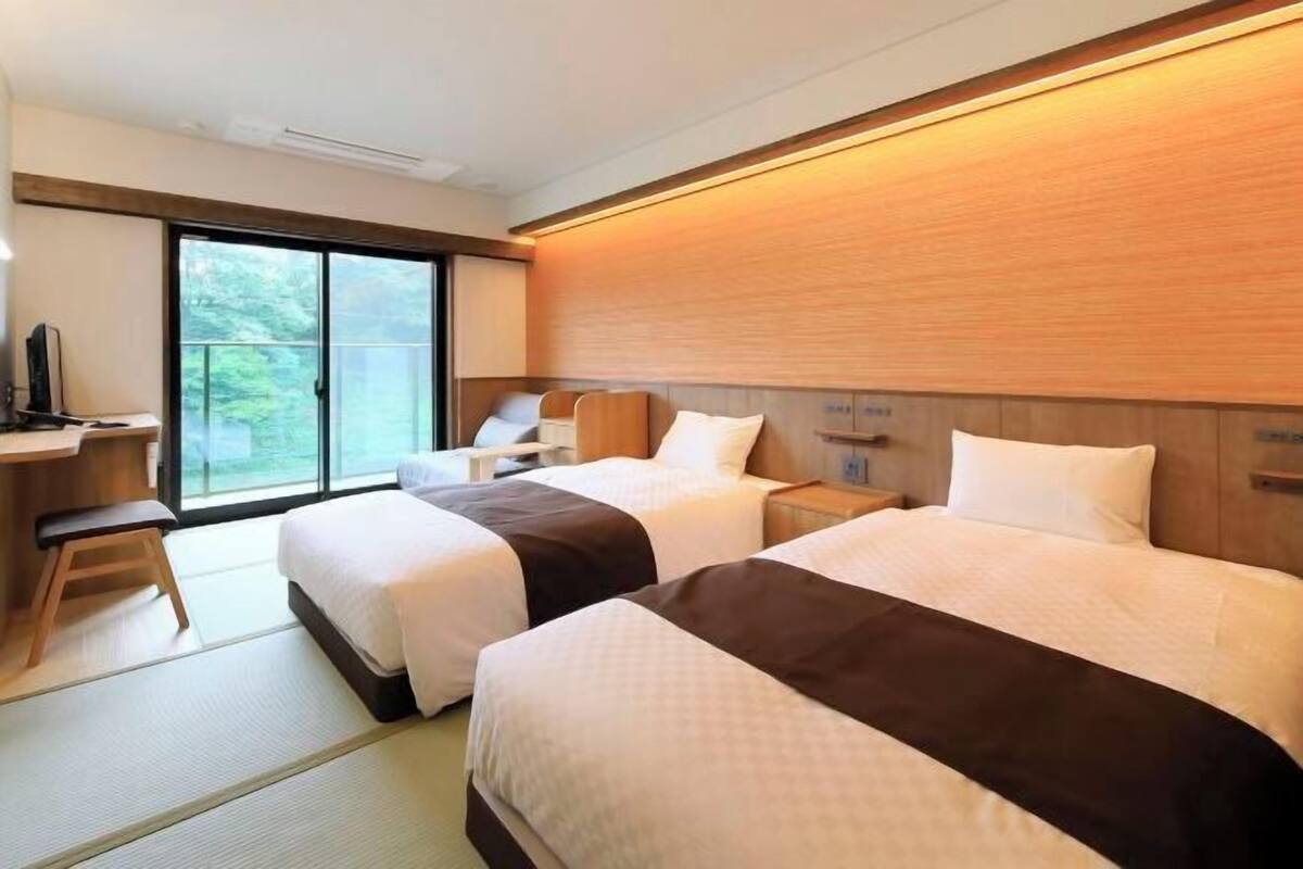 A hotel room with two beds, a desk, and a sliding glass door to the outside.