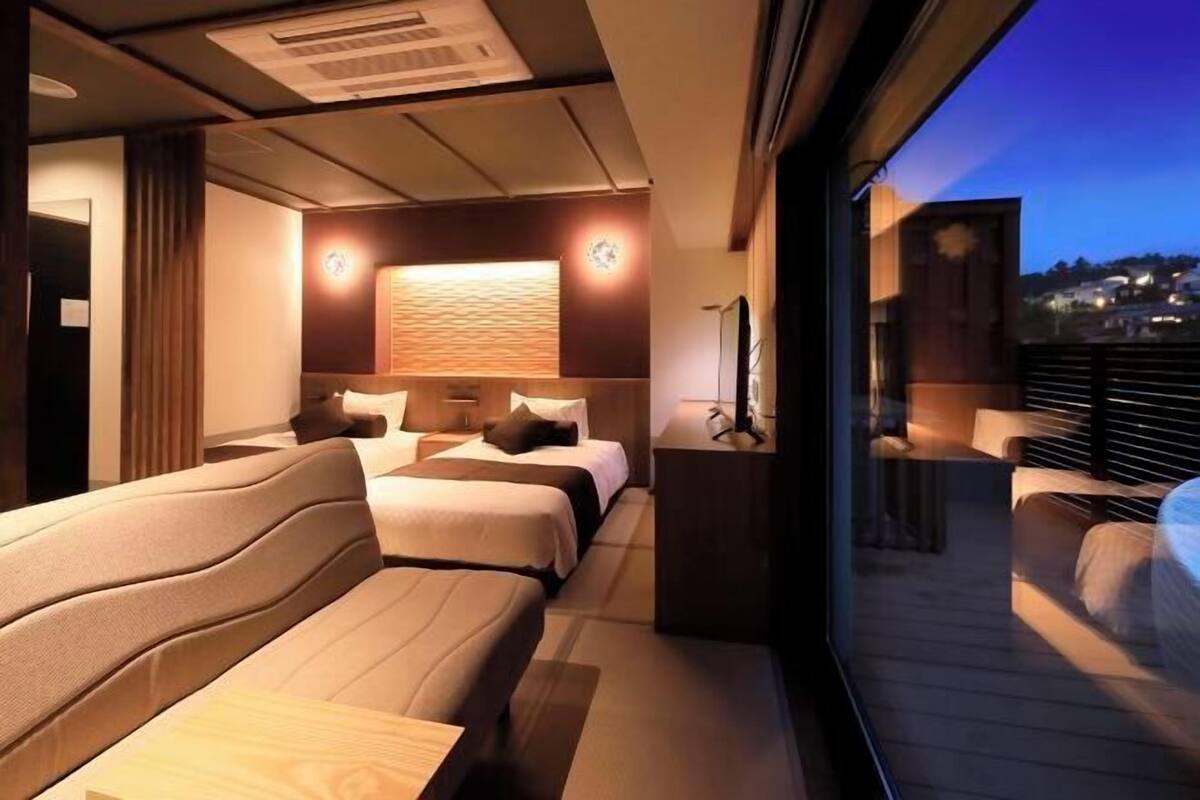 A modern hotel room with a balcony, a large bed, a sofa, and a wall-mounted TV.