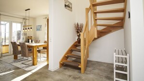 Un intérieur moderne avec un escalier en bois, un coin repas comprenant une table et des chaises, et un vase contenant des plantes séchées.
