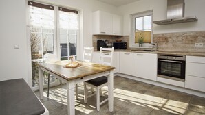 Une cuisine moderne avec des meubles blancs, une table à manger en bois et un four encastré.