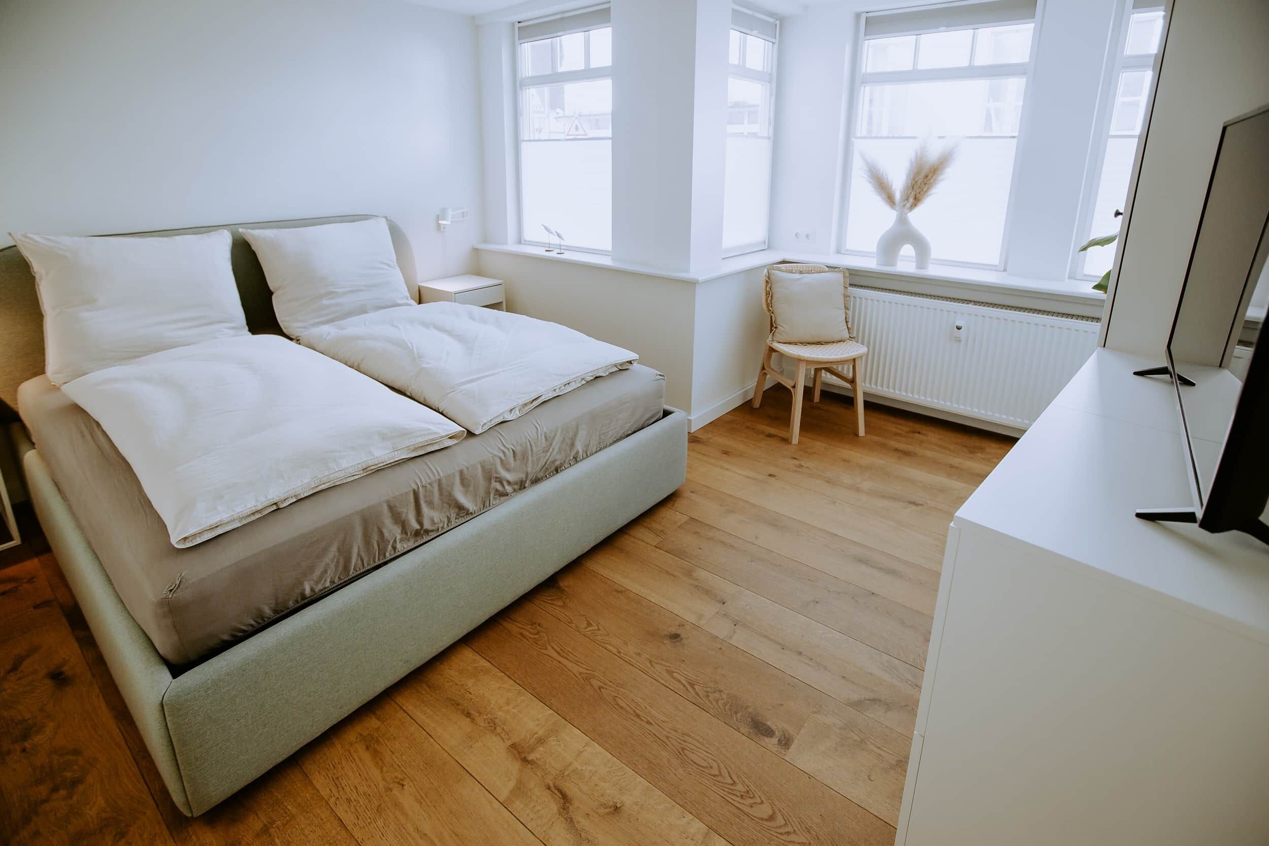 A minimalist bedroom with a bed, a chair, a desk, and a large window.