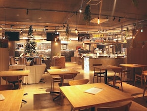 Un restaurante acogedor con mesas y sillas de madera, una zona de bar con un letrero que dice 'SWEETS' y un árbol de Navidad.
