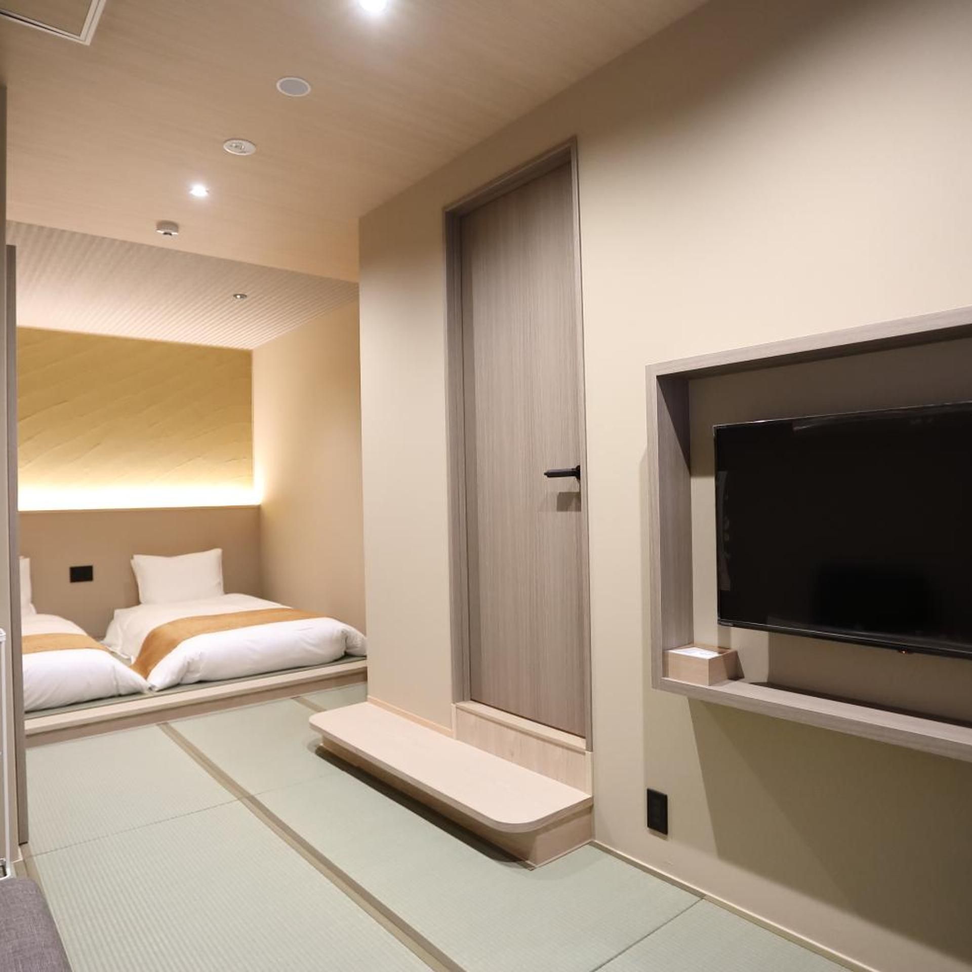 Quarto de hotel com duas camas, televisão e porta de correr.