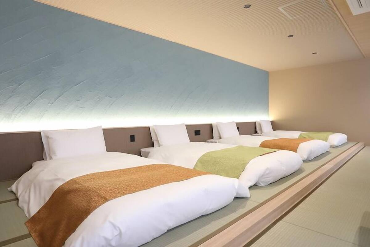 A hotel room with three beds, a large wall mural, and a modern ceiling design.