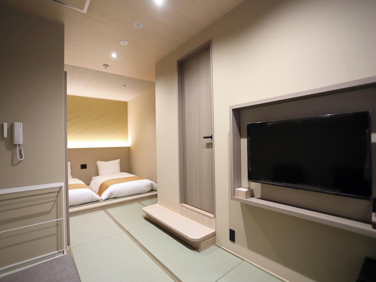 Een hotelkamer met een bed, een televisie, een telefoon en een klein zithoekje.