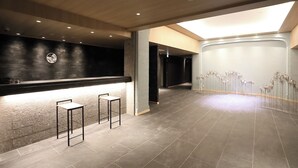 A modern lobby with a reception desk, two bar stools, a wall clock, and a decorative floral arrangement. - Miyawaka Torano Yu (Miyawaka)