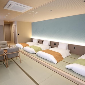 A hotel room with a bed, bedside tables, a chair, and a wall-mounted air conditioning unit. - Miyawaka Torano Yu (Miyawaka)