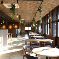 Un espacio interior amplio con mesas y sillas, ventanas grandes y plantas colgantes.