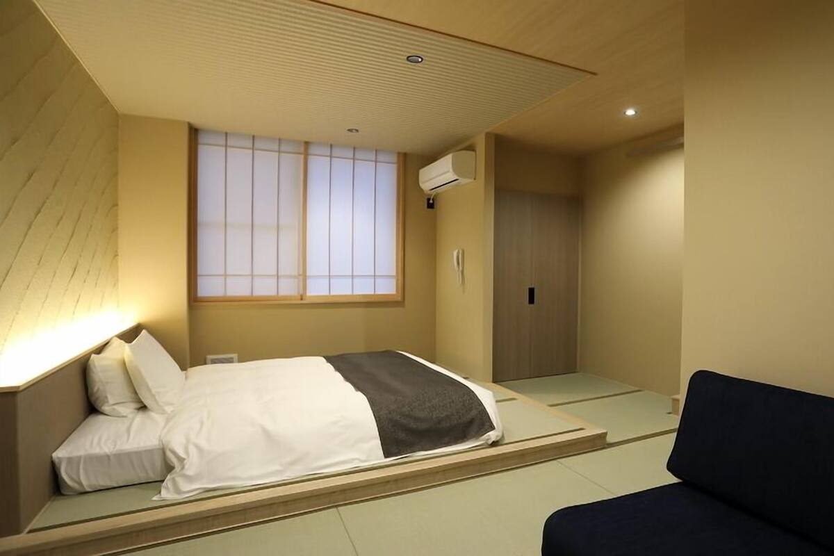 A modern bedroom with a bed, a sofa, a window with blinds, and a ceiling fan.