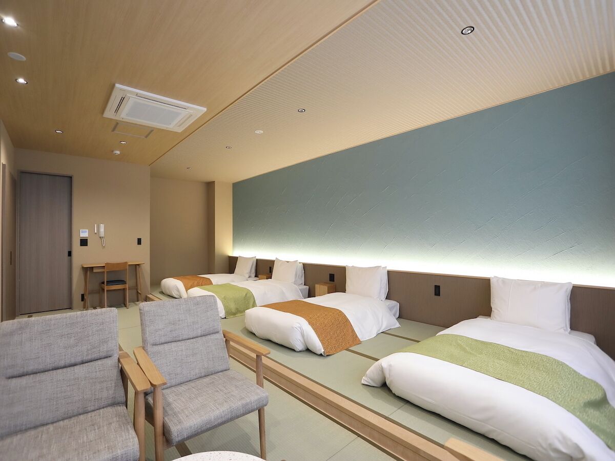 Een hotelkamer met drie bedden, een bureau en twee stoelen.