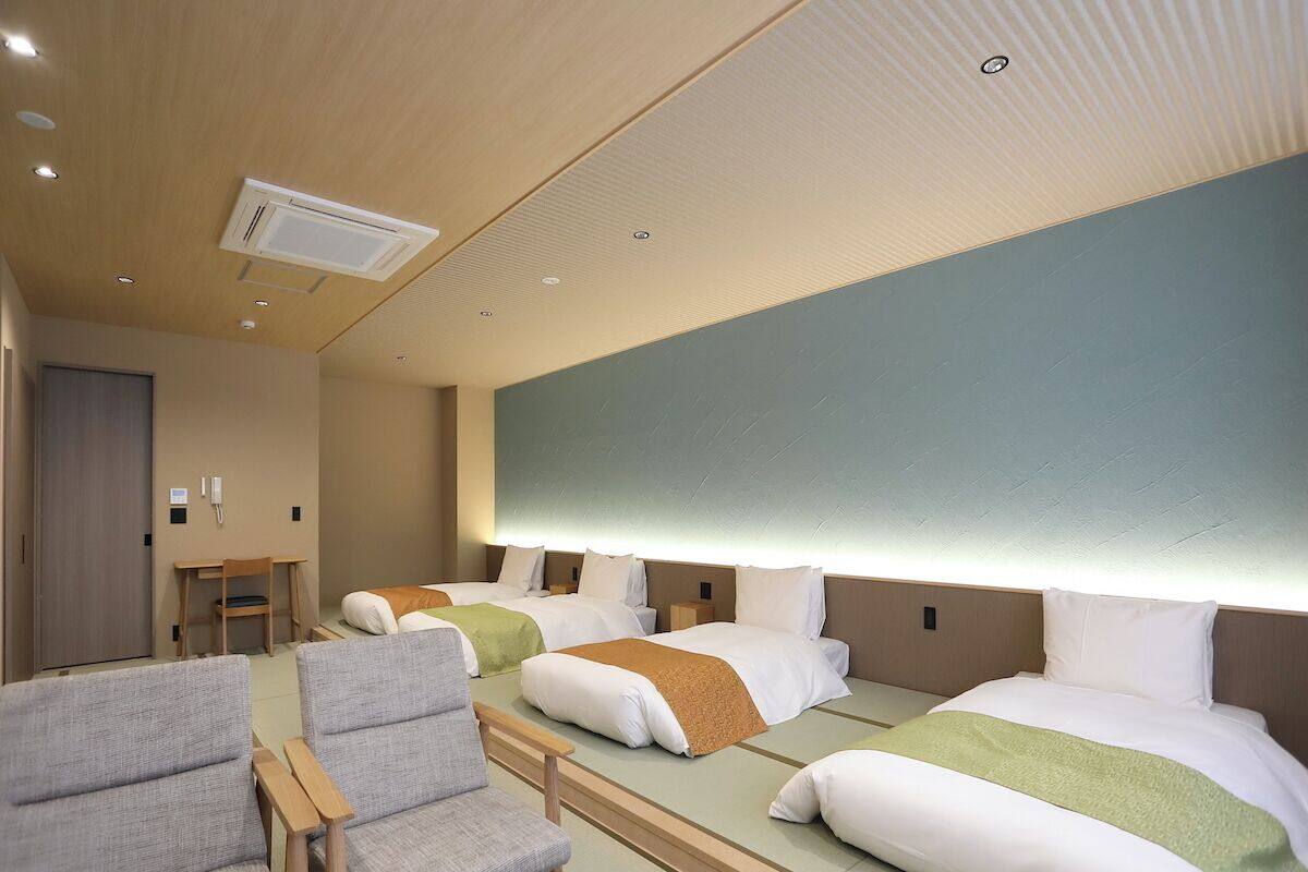 A hotel room with three beds, a desk, and two chairs.