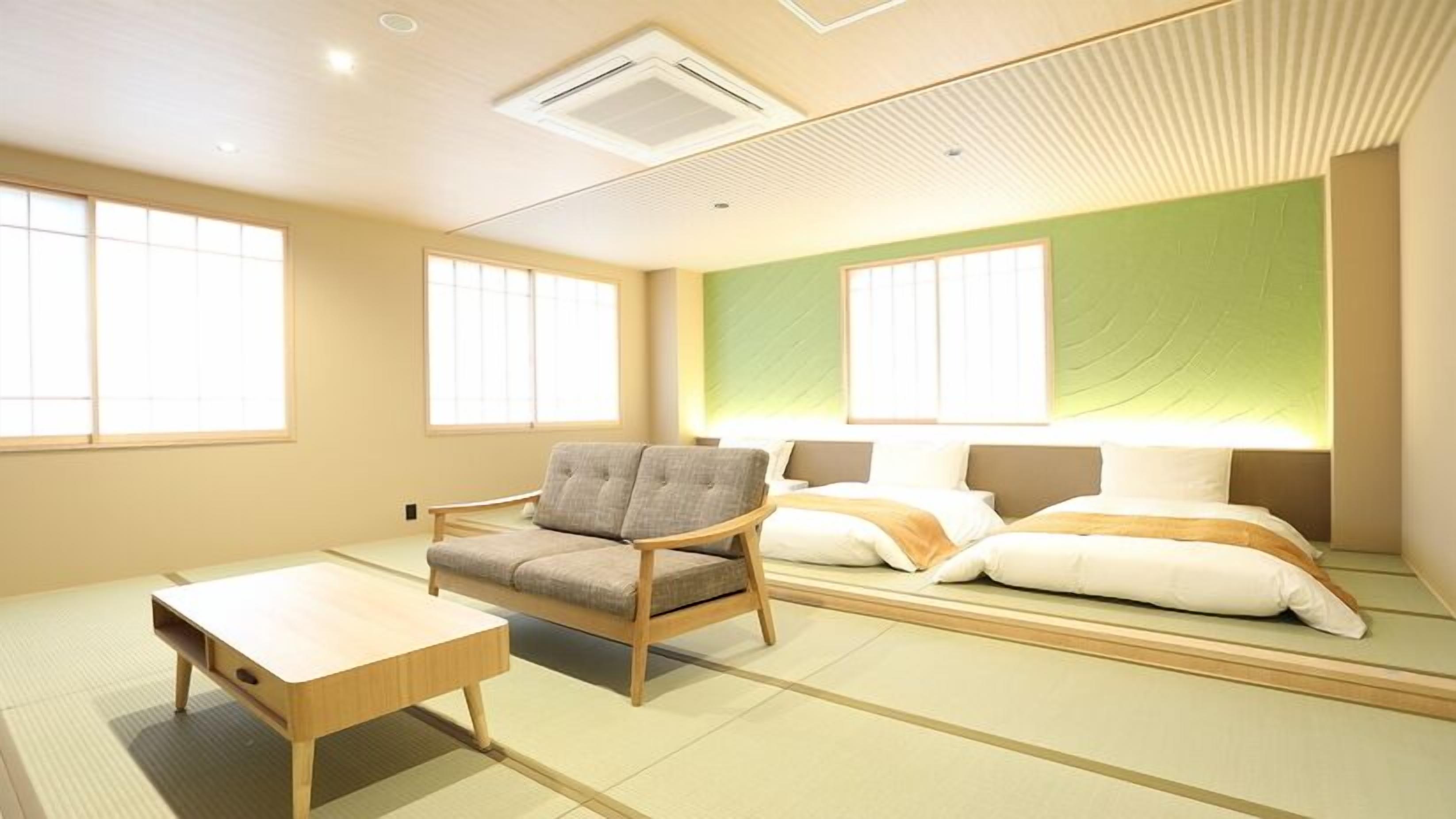 A room with tatami flooring, a low wooden table, a cushioned chair, and a bed with pillows.