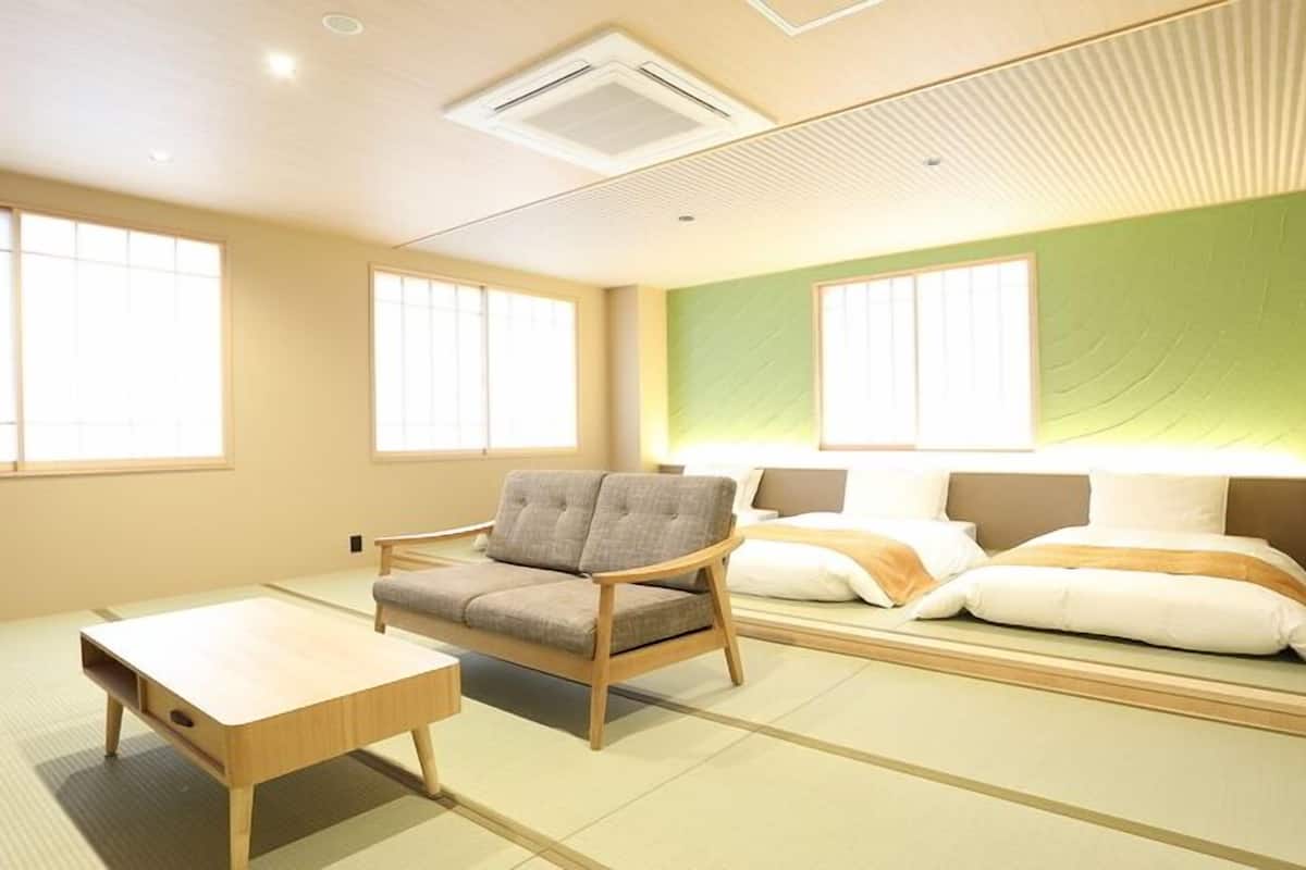 A room with tatami flooring, a low wooden table, a cushioned chair, and a bed with pillows.