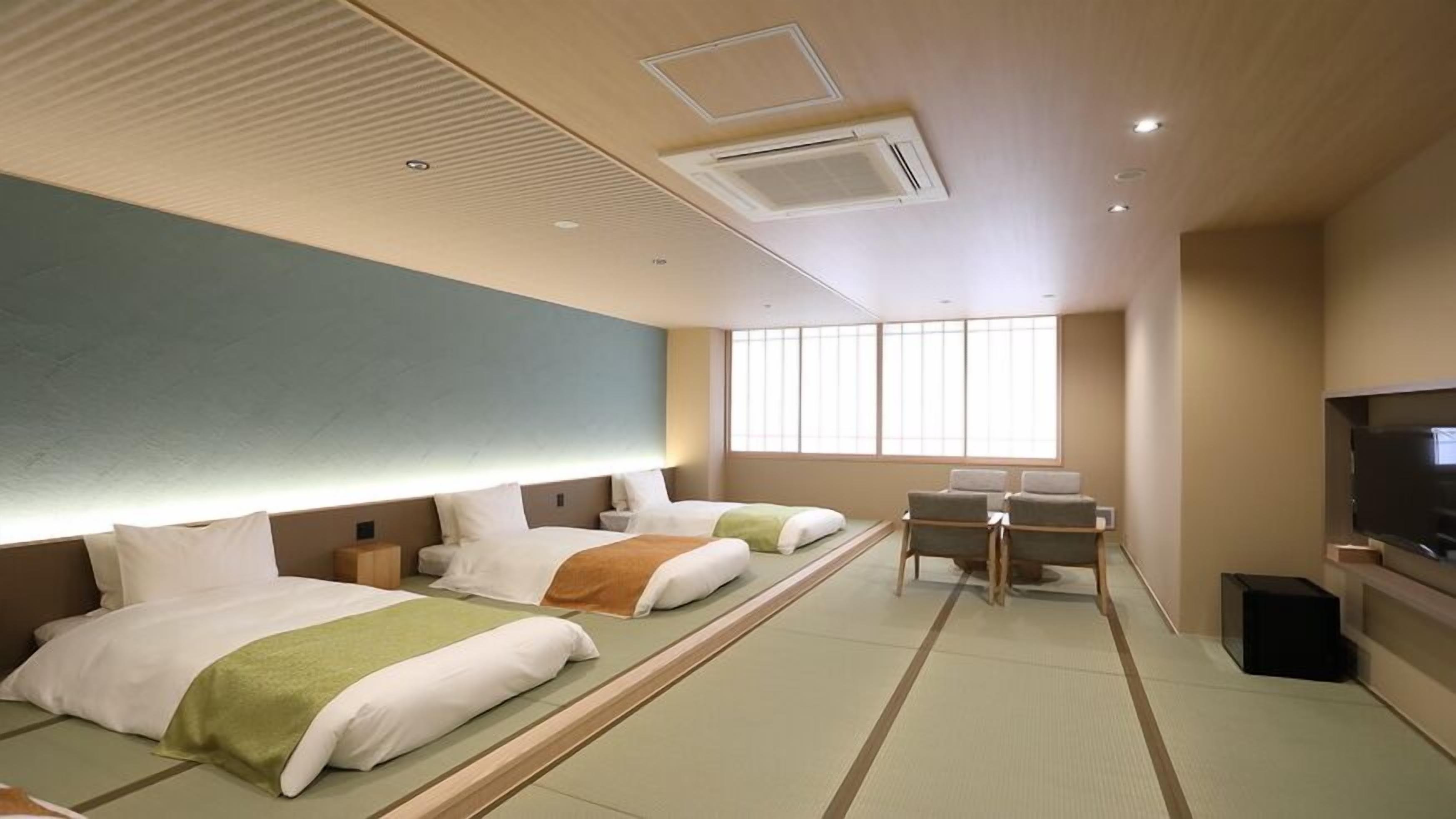 A hotel room with two beds, a desk, a television, and a large window.