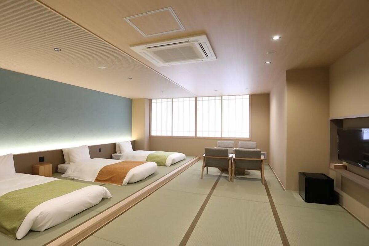 A hotel room with two beds, a desk, a television, and a large window.