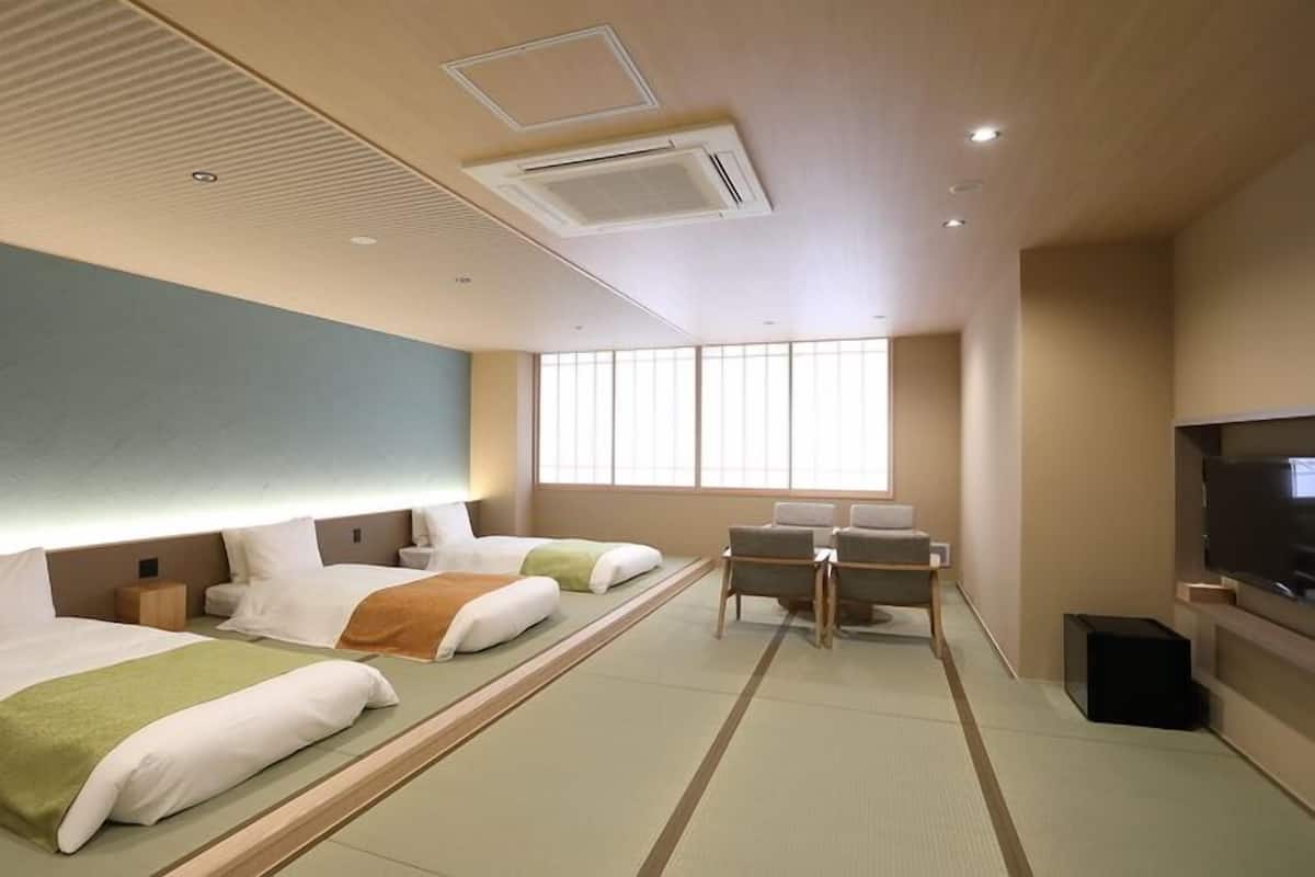 A hotel room with two beds, a desk, a television, and a large window.