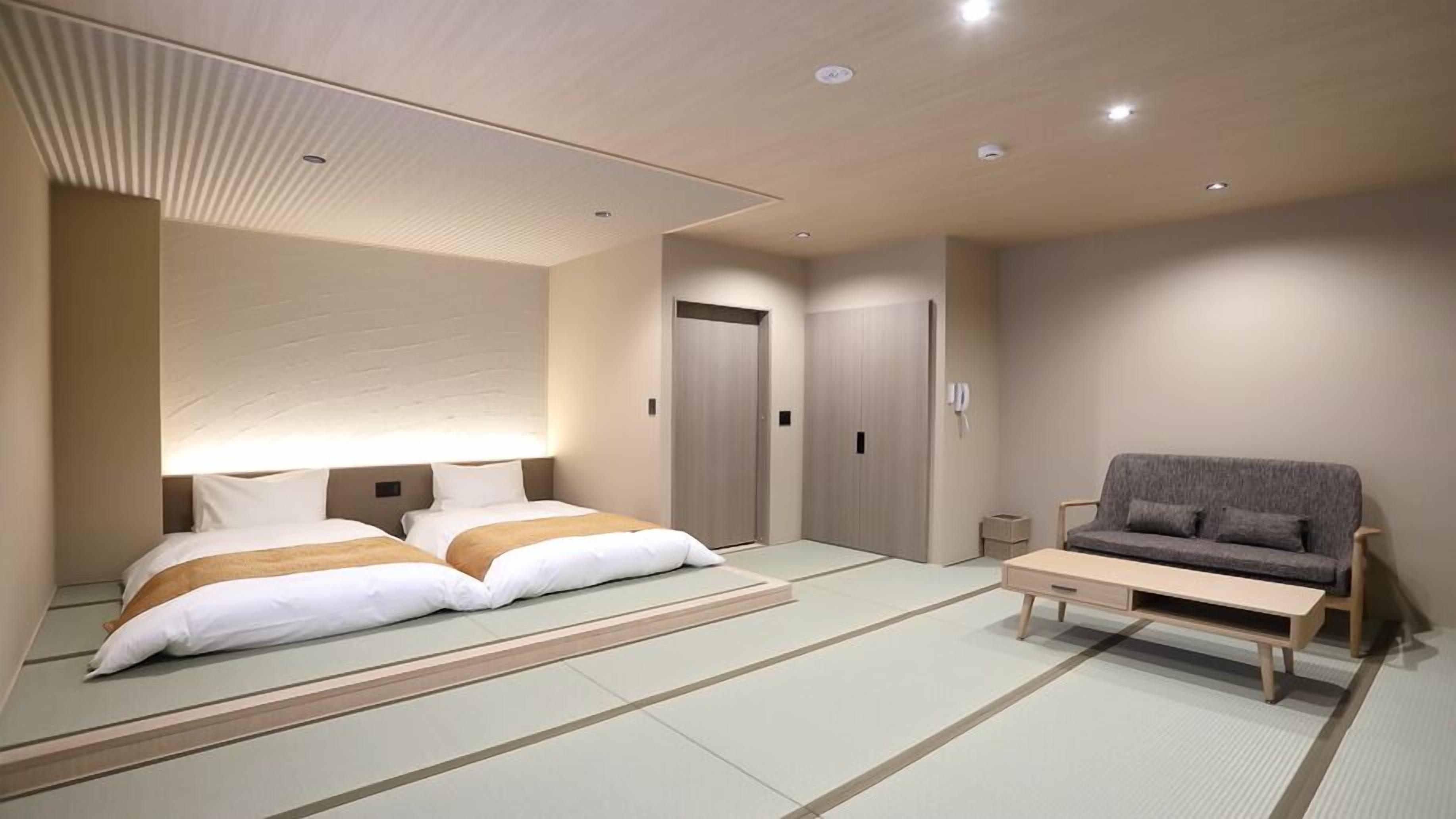 A hotel room with two beds, a sofa, a small table, and a traditional tatami mat floor.