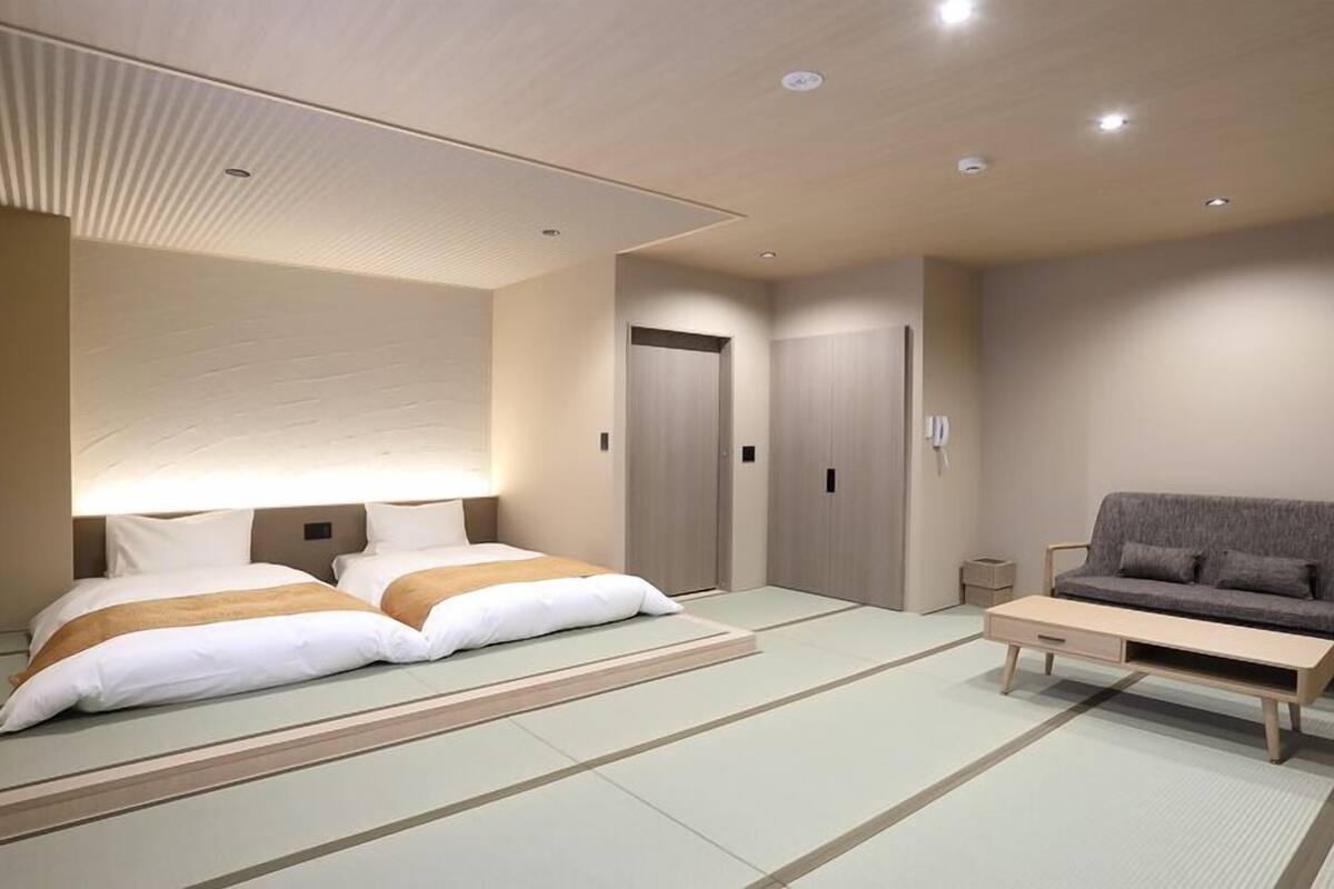 A hotel room with two beds, a sofa, a small table, and a traditional tatami mat floor.