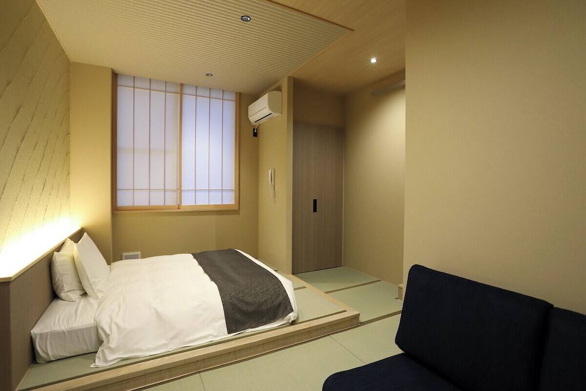 A hotel room with a bed, a sofa, a sliding door, and a window with a view.