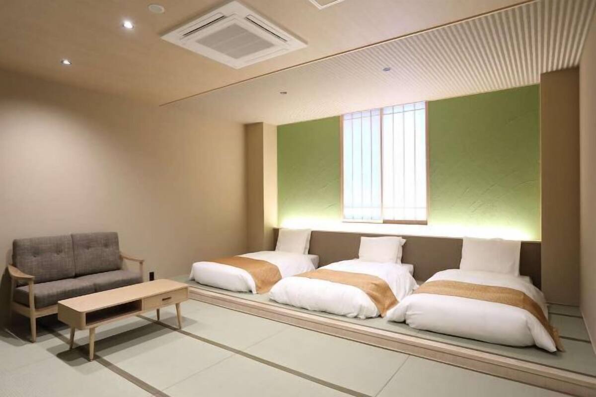 A hotel room with a sofa, two beds, a small table, and a large window.