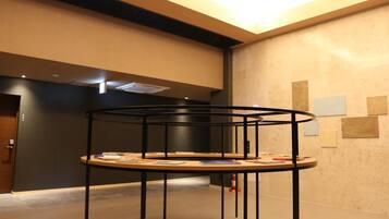 A modern interior with a central black metal table surrounded by books and papers, a dark wall with a door, and a ceiling with recessed lighting.