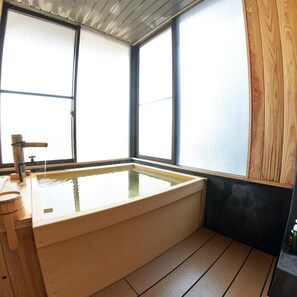 Quarto com uma banheira grande, piso de madeira e janela com vista.