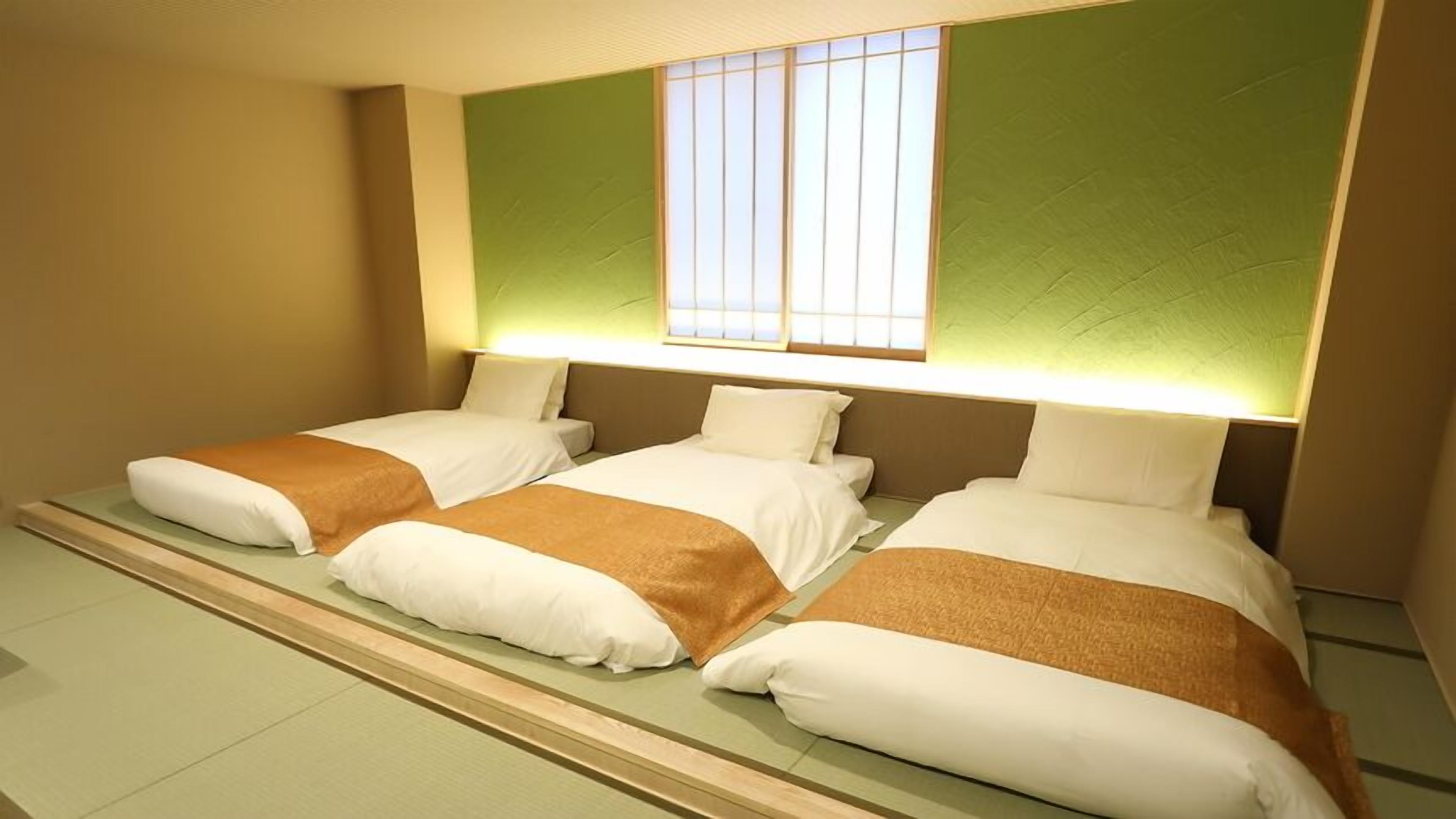 A hotel room with three beds, a large window, and a green accent wall.