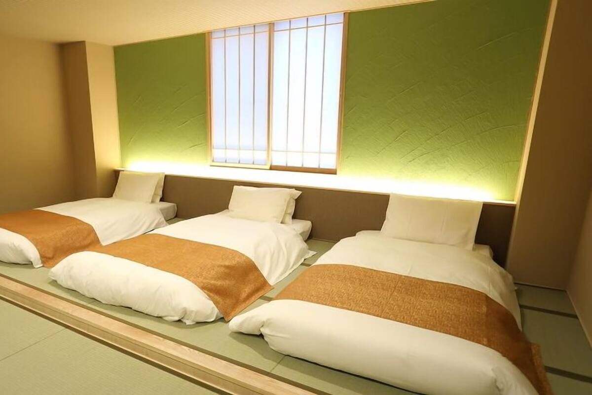 A hotel room with three beds, a large window, and a green accent wall.