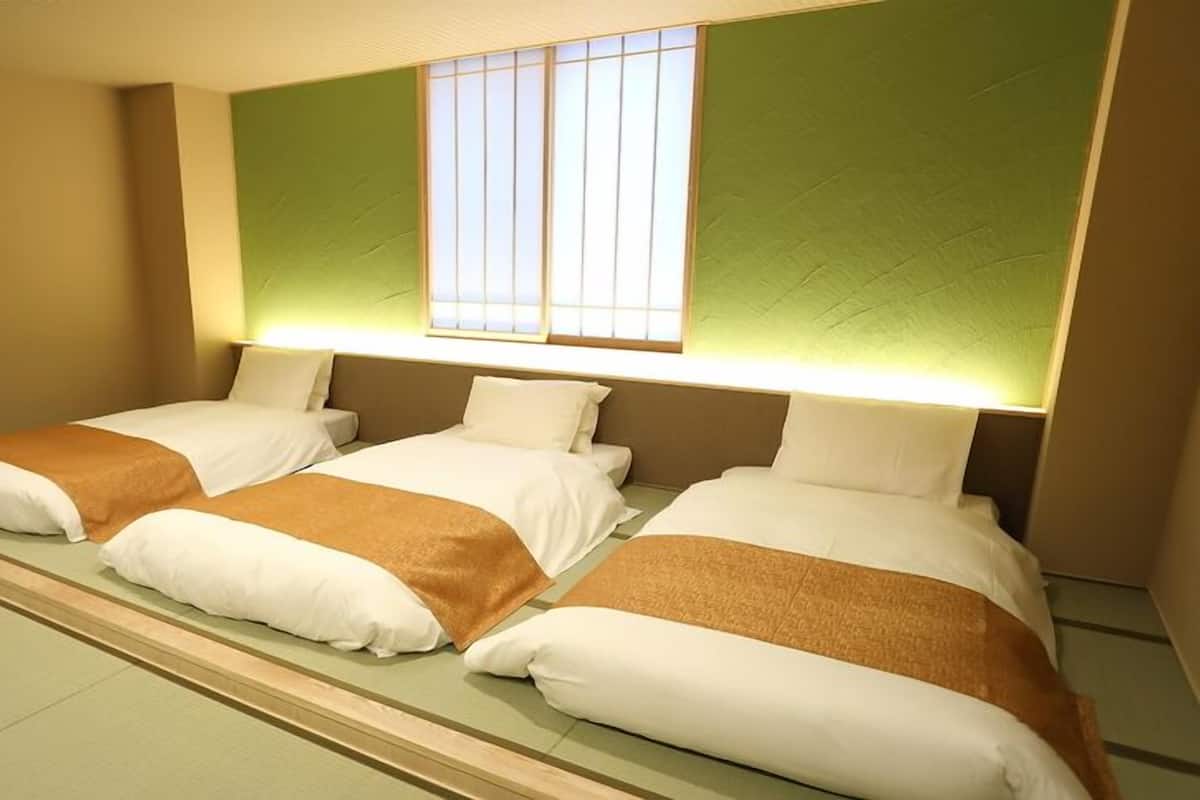 A hotel room with three beds, a large window, and a green accent wall.