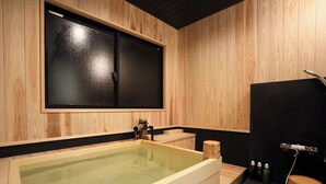 A wooden spa room with a large bathtub, a wooden bench, and a black cabinet. - Miyawaka Torano Yu (Miyawaka)