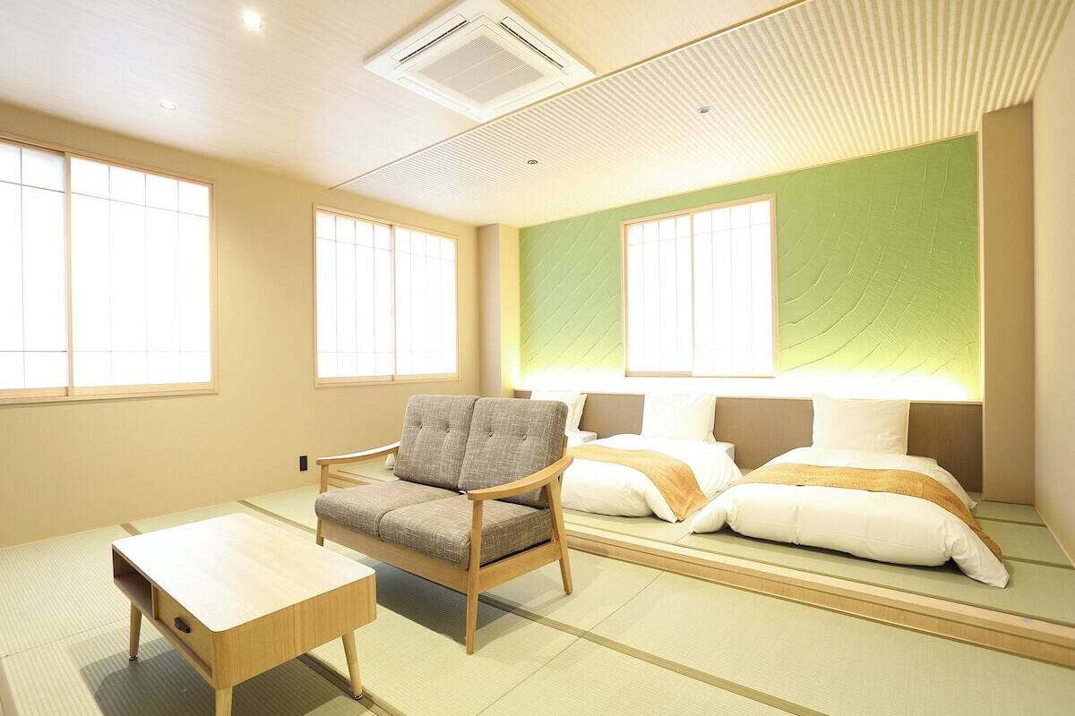 A room with tatami flooring, a sofa, a bed with pillows, a small table, and a wall-mounted air conditioner.